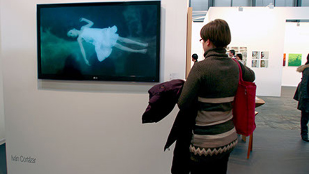 A woman at the ARCO art fair stares at a TV displaying an image of a child sleeping underwater